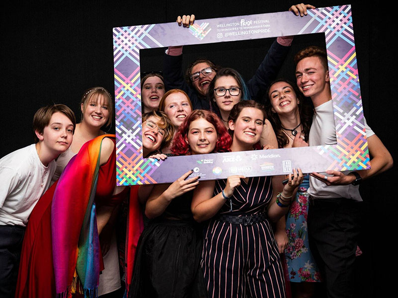 Inside OUT Youth Ball. A diverse group of people posing for a photo with an oversized frame.
