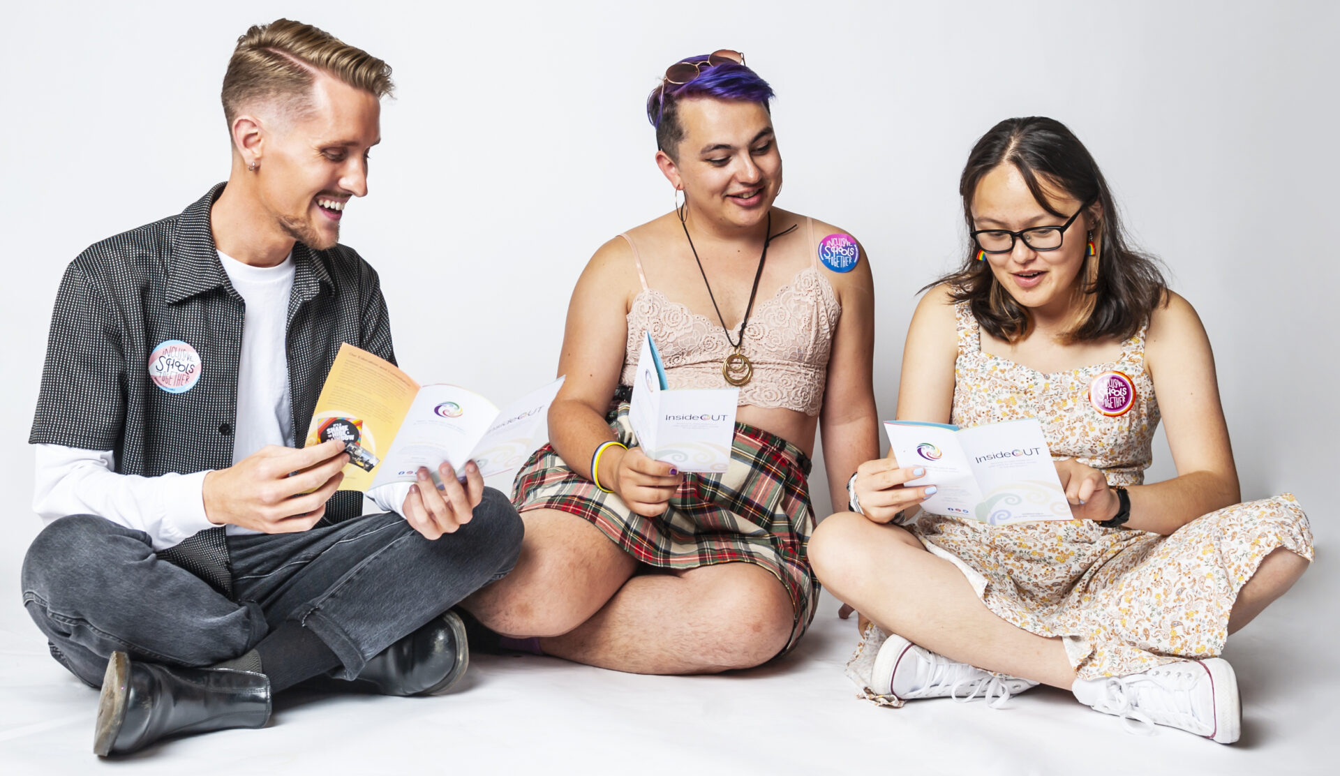 Inside OUT opportunities. A studio portrait photograph of three seated diverse people reading brochures and leaflets.