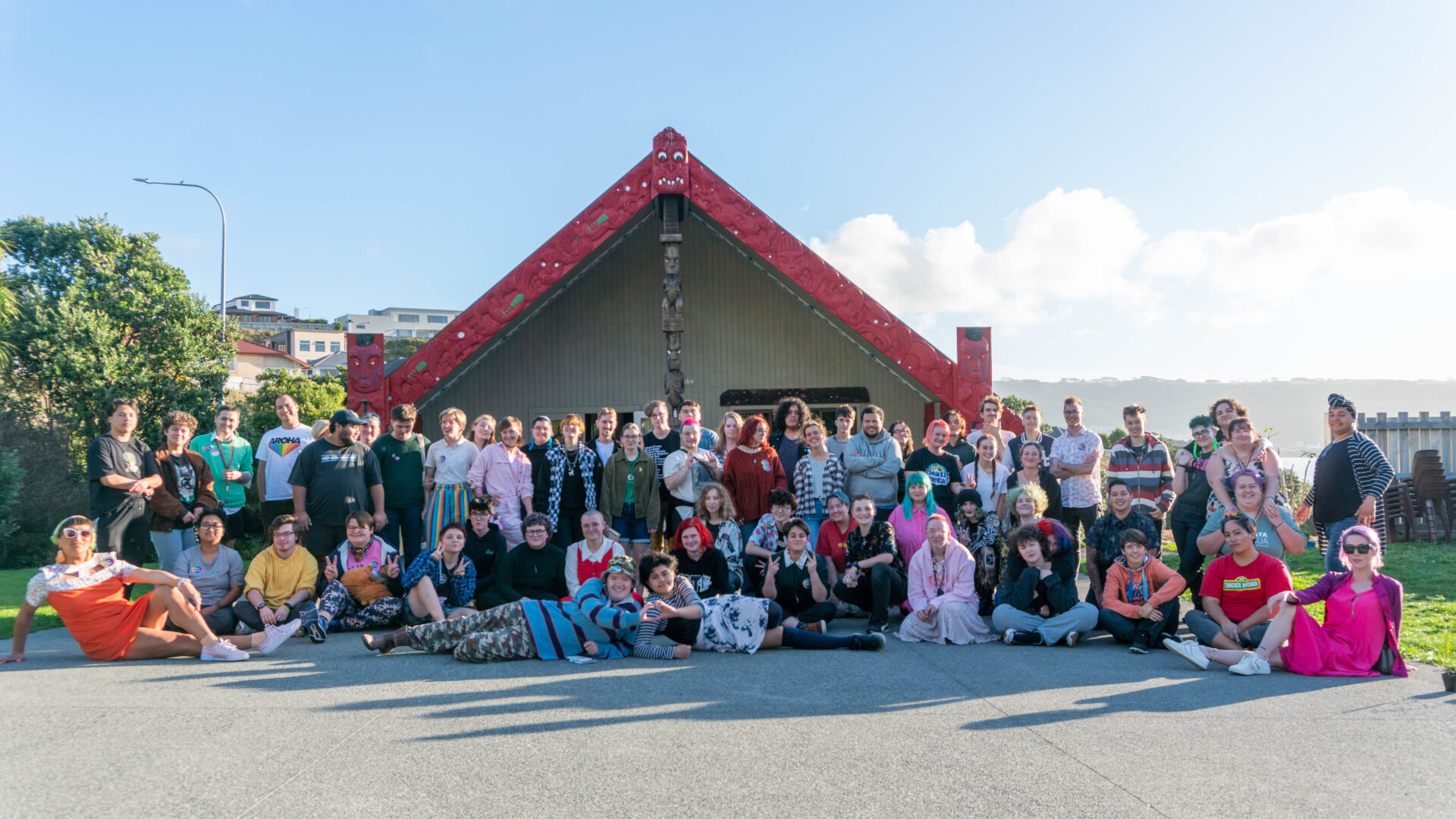 ShiftHui InsideOUT A diverse group of people gathered outside the wharenui of Horouta Marae on a sunny day.