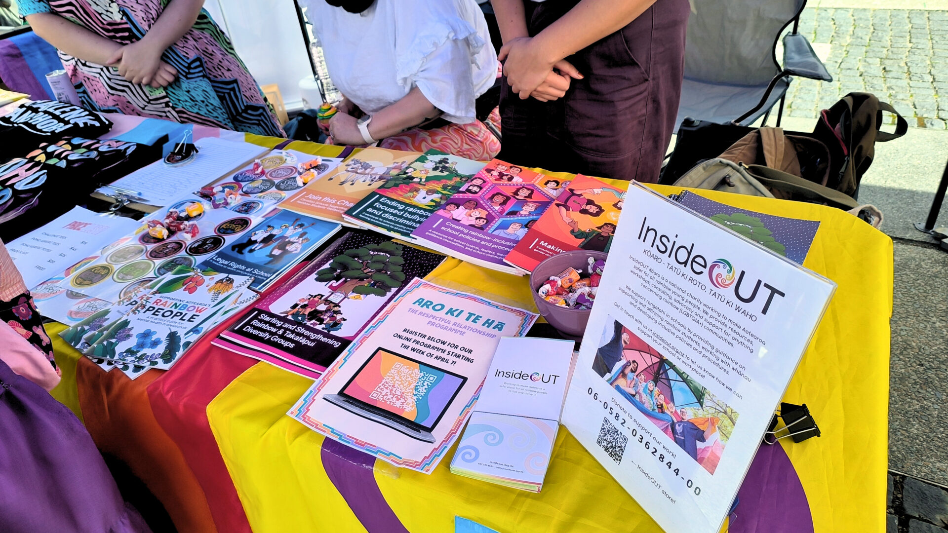 A table with a range of resources, stickers, and other merchandise for Inside Out. The table is covered with pride flags, with a sign with information on Inside Out.